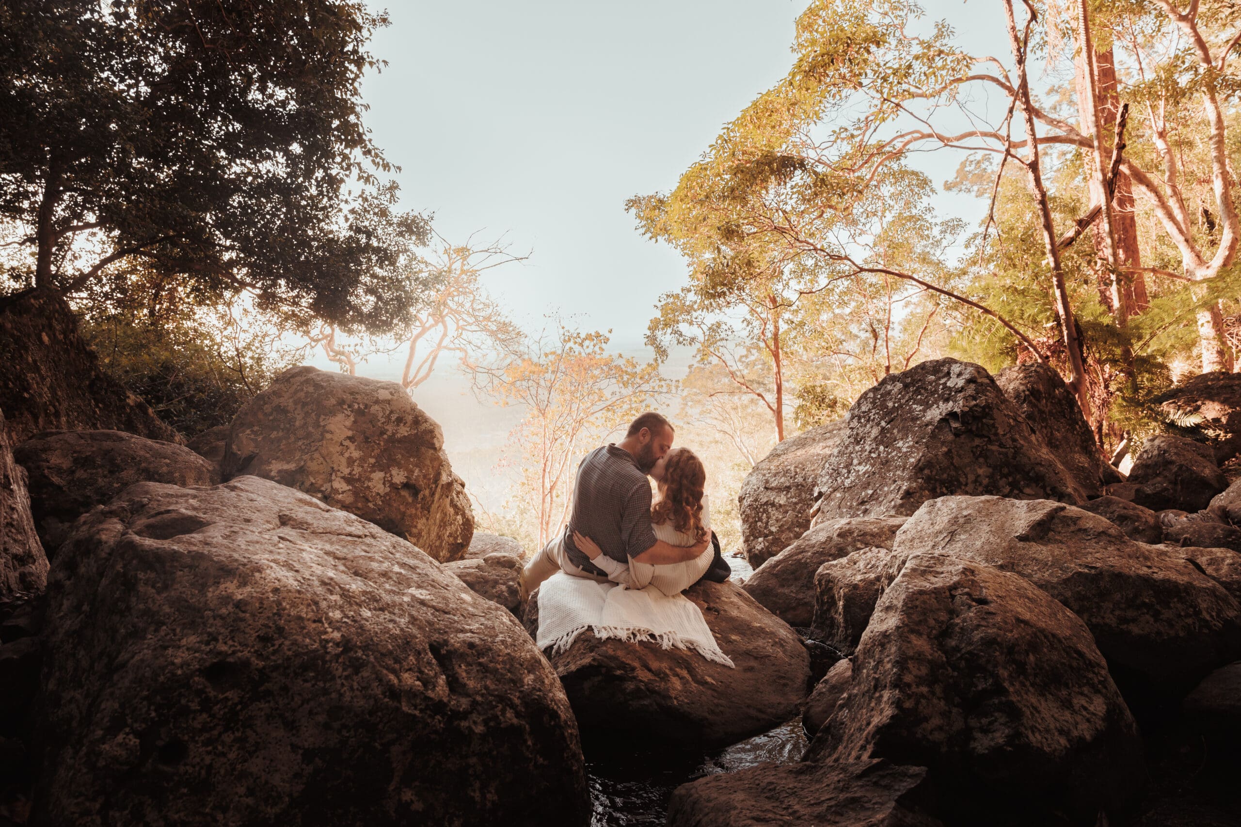 Romantic couple kissing at Mount Tamborine summit during golden hour – Brisbane couples photoshoot with scenic mountain views.