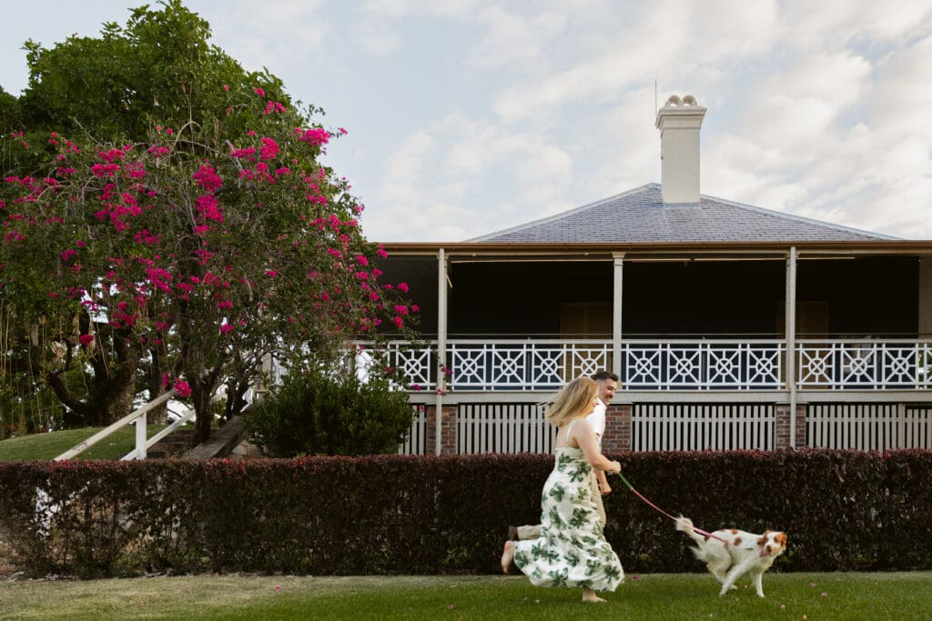 Engaged couple walking their dog during a relaxed engagement photoshoot at Newstead House, Brisbane, captured by a Brisbane wedding photographer in a natural documentary style.