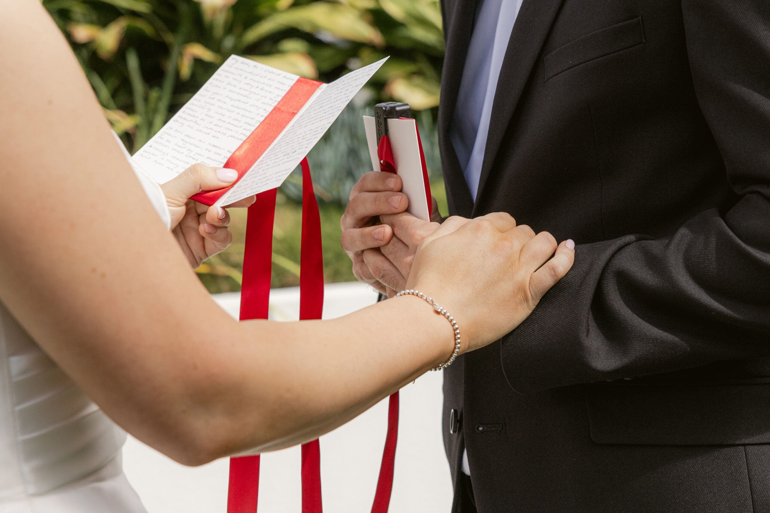 Close-up of a bride reading handwritten wedding vows while holding the groom’s hand during an outdoor ceremony.