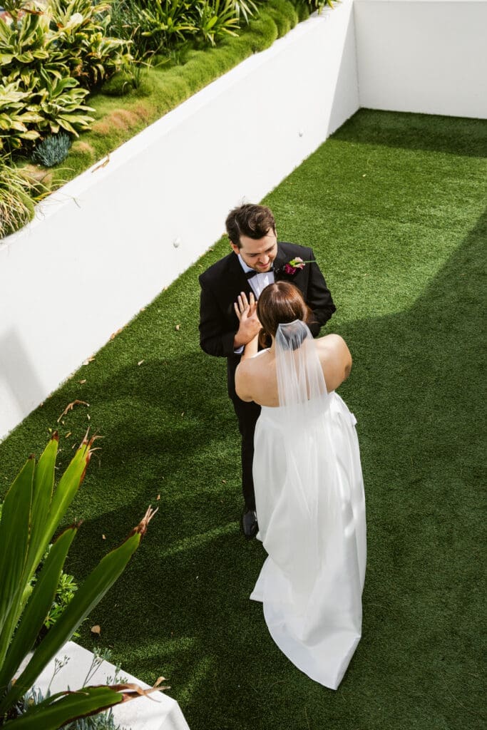 Bride and groom exchanging vows during an intimate outdoor wedding ceremony in a modern garden setting with white architectural walls and greenery.